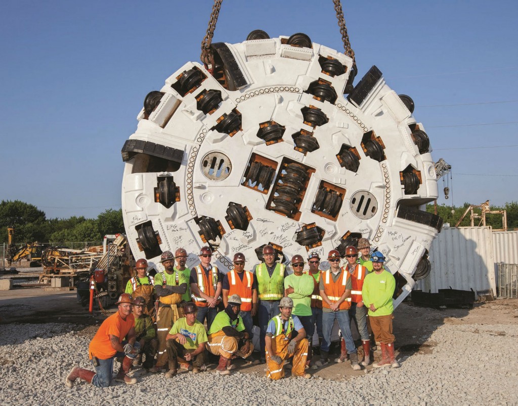 The S-K JV stands proudly in front of the cutterhead for the 6.2 m (20.2 ft) diameter Robbins TBM currently boring the DigIndy tunnels. The S-K JV stands proudly in front of the cutterhead for the 6.2 m (20.2 ft) diameter Robbins TBM currently boring the DigIndy tunnels.