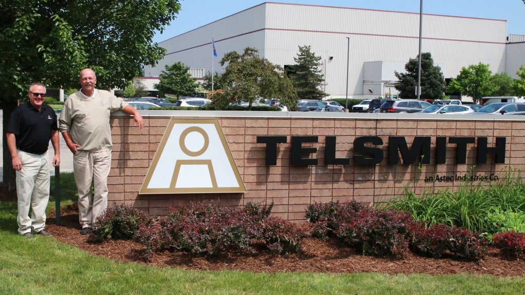 Two men standing next to a Telsmith sign