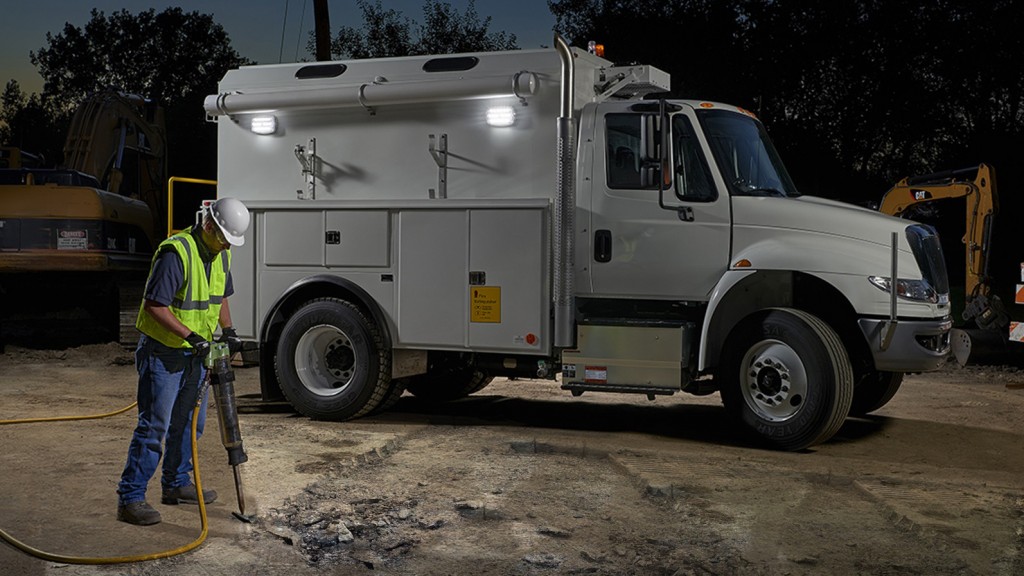 worker drills a hole in the ground in front of a truck