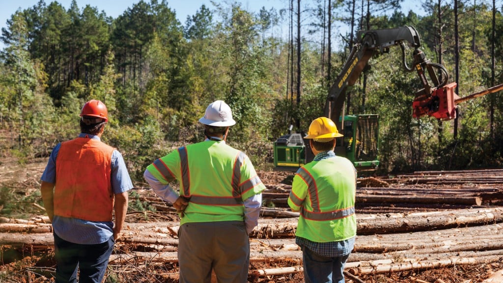 Forestry workers look on as logging machine picks up log