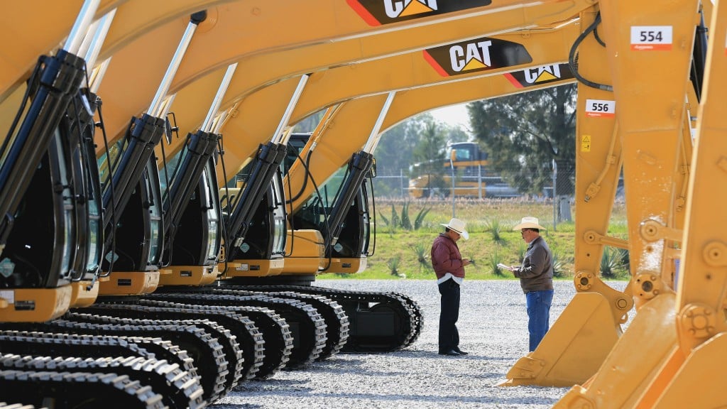 two men stand underneath a row of caterpillar machines