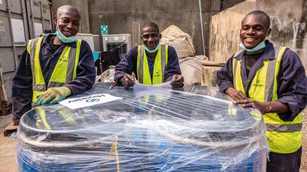 three workers stand in front of a load of wrapped drums