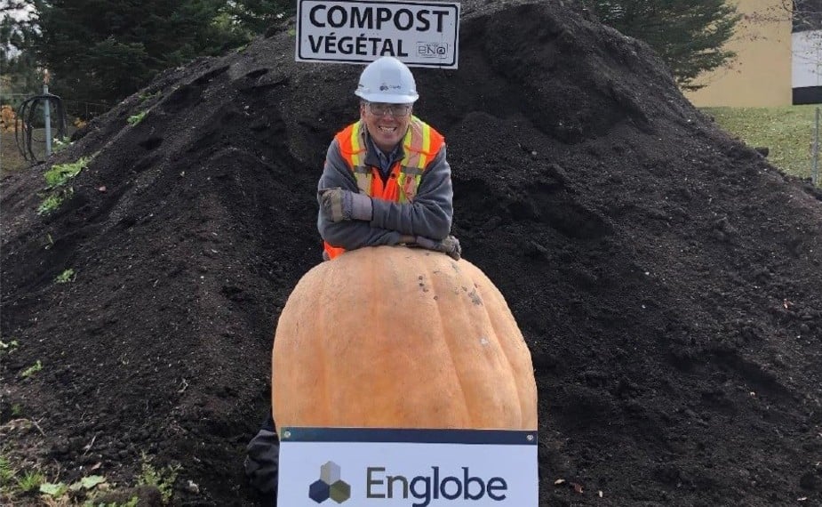 Englobe worker stands proudly with large pumpkin in compost heap