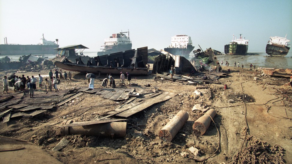 people walk on a beach strewn with rubble and refuse