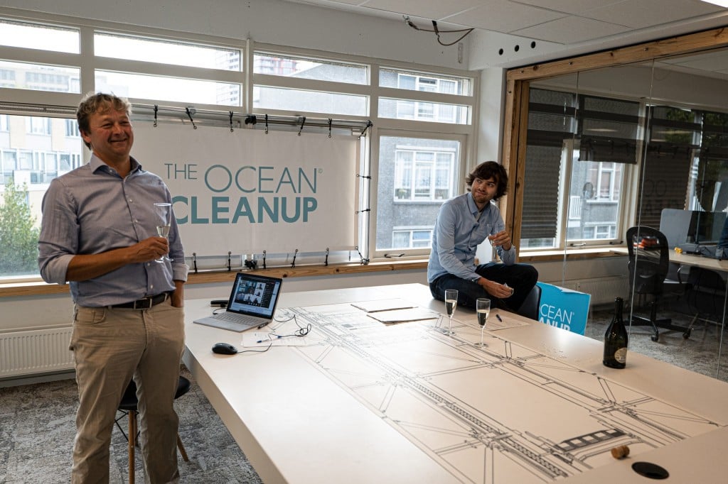 two men stand next to a table with The Ocean Cleanup banner in background