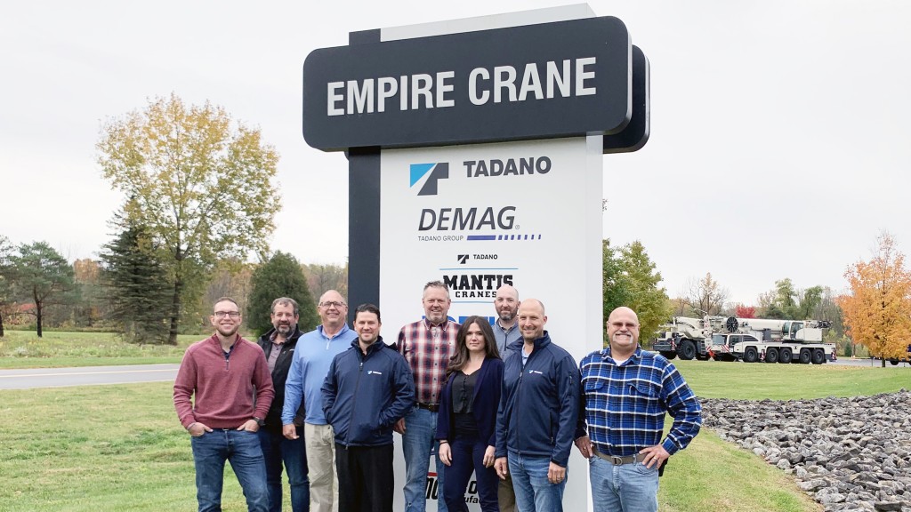 Empire Crane and Tadano representatives stand underneath Empire Crane sign  