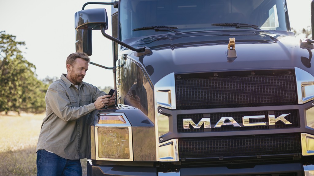 man texts on phone next to Mack truck