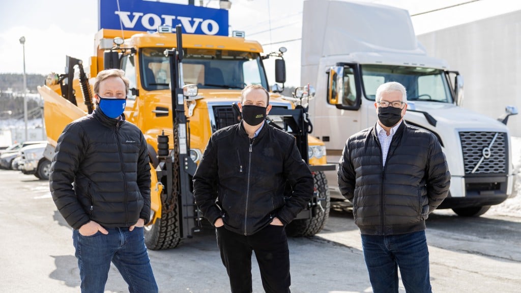 3 men in masks stand in front of Volvo truck