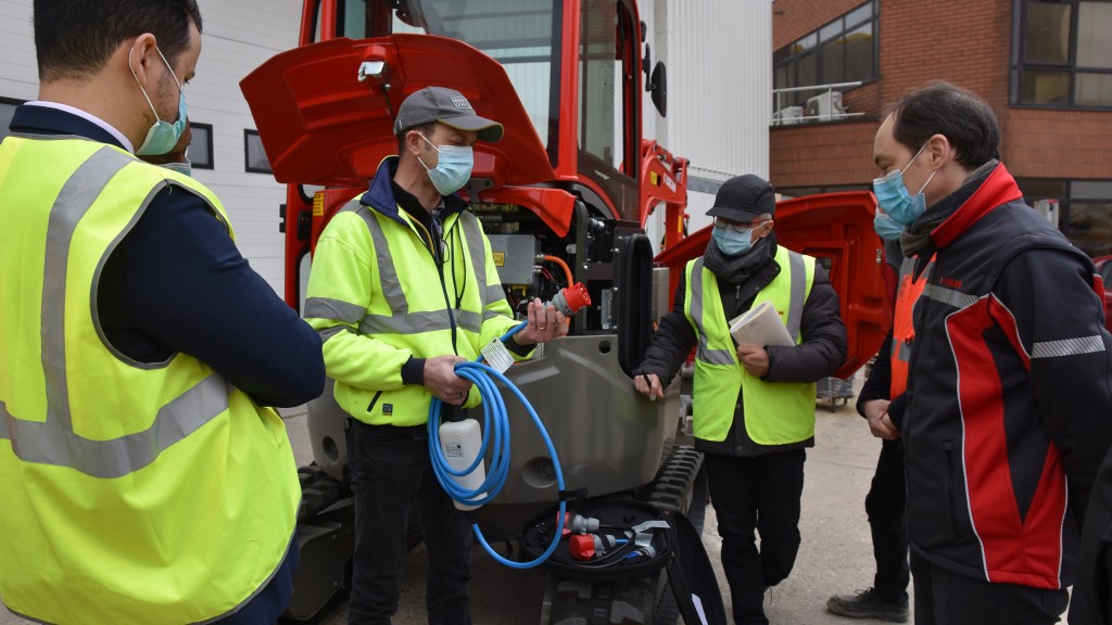 Technicians in masks discuss in front of a machine