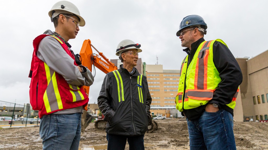 three workers in front of Hitachi excavator