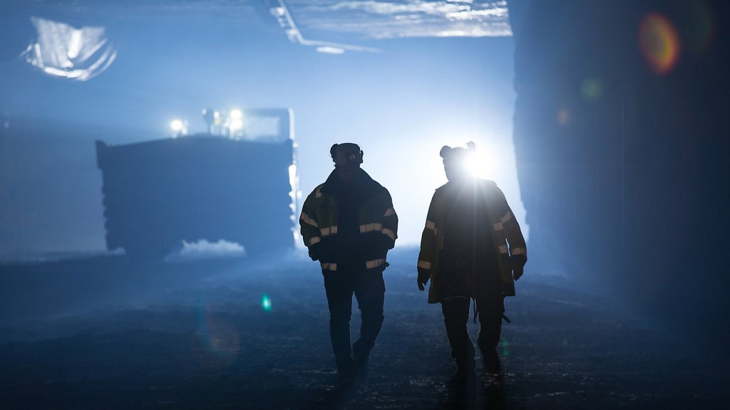 two workers walking in underground mining site with scoop tram st14 in background