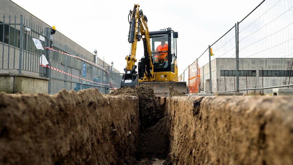 A Cat mini hydraulic excavator digs a trench on a job site