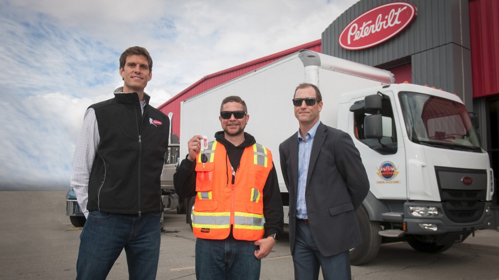 Three men pose in front of a Peterbilt Model 220EV