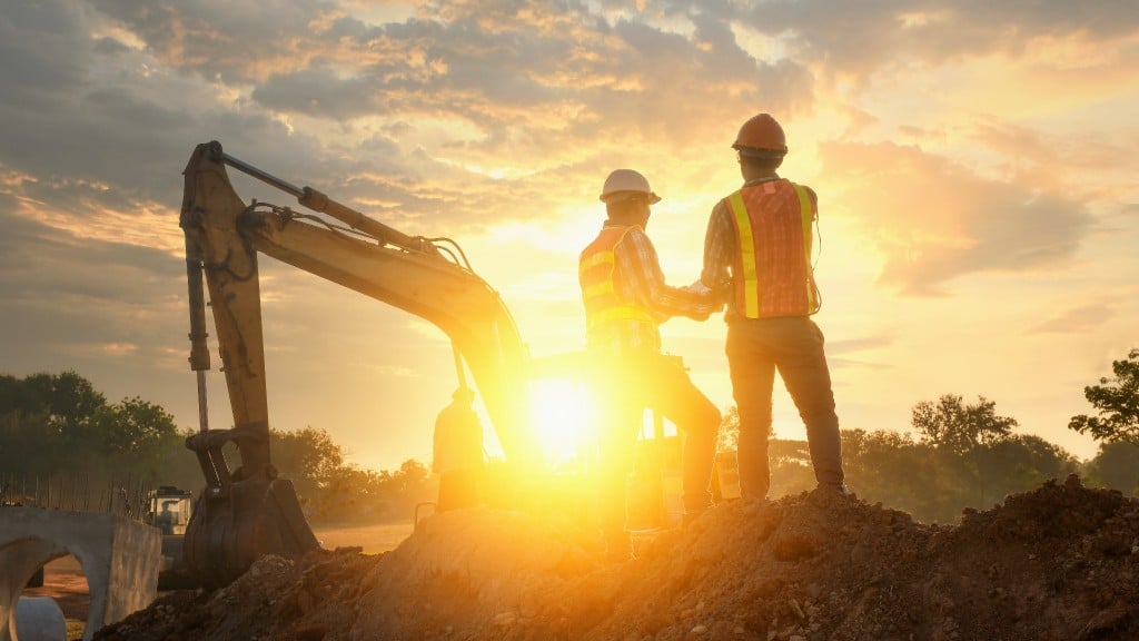 Two construction workers handsake infront of the glowing sun