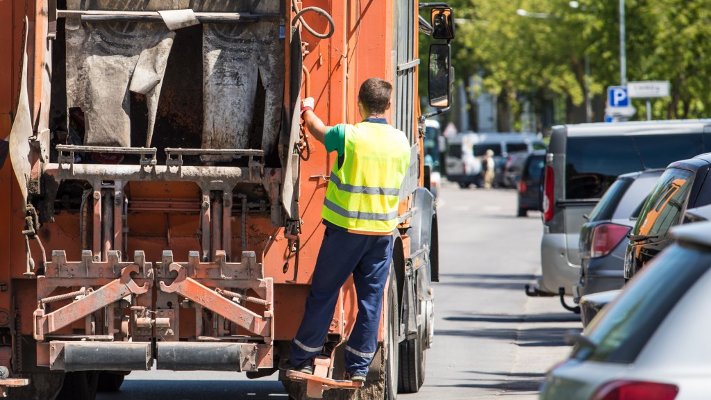 A worker rides on the back of a collection truck