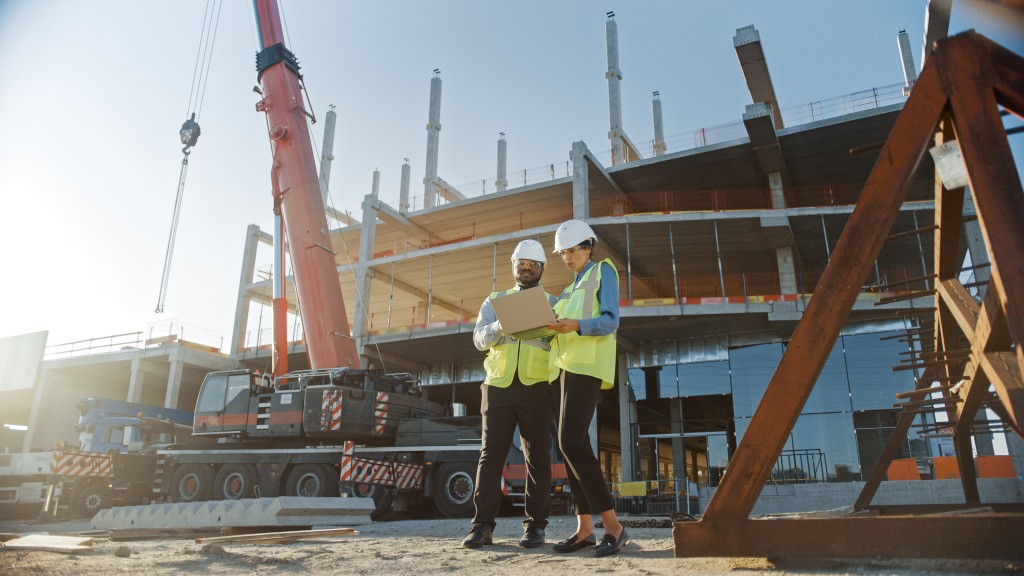 Two workers look at a laptop on a job site