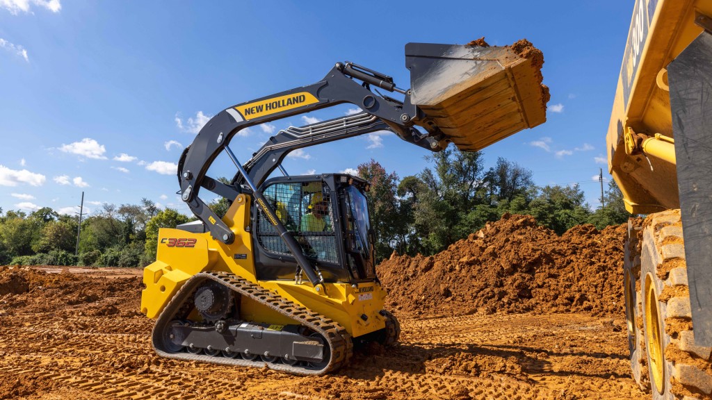 A compact track loader fills a truck with dirt