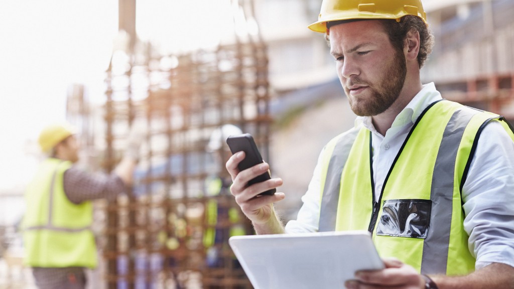 Construction worker texting while holding tablet on job site