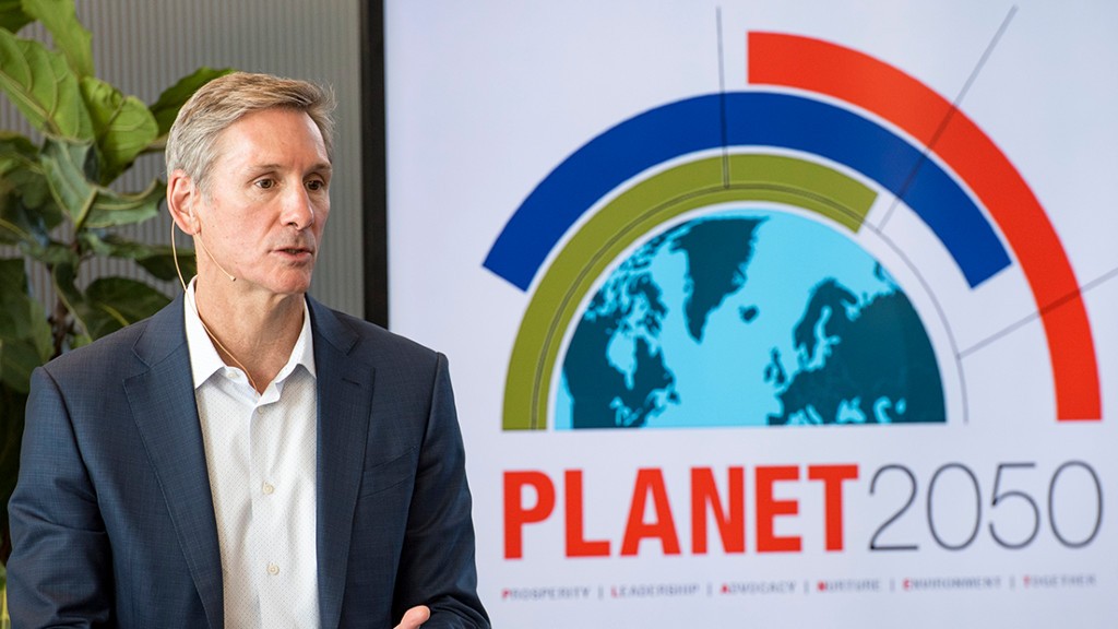 A host talks in front of a PLANET 2050 poster