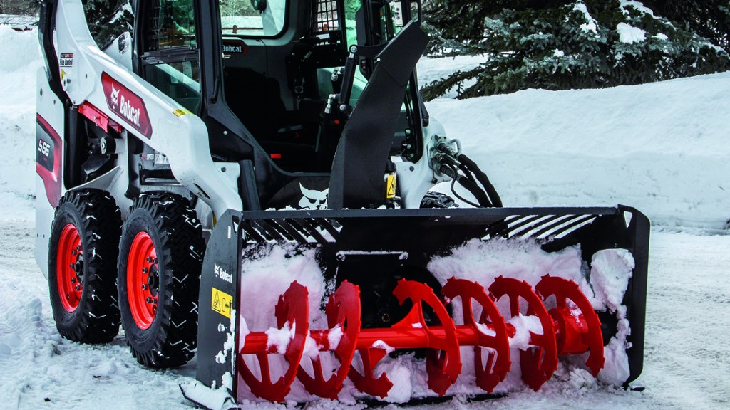 A snowblower equipped skid steer loader clears snow on the job site