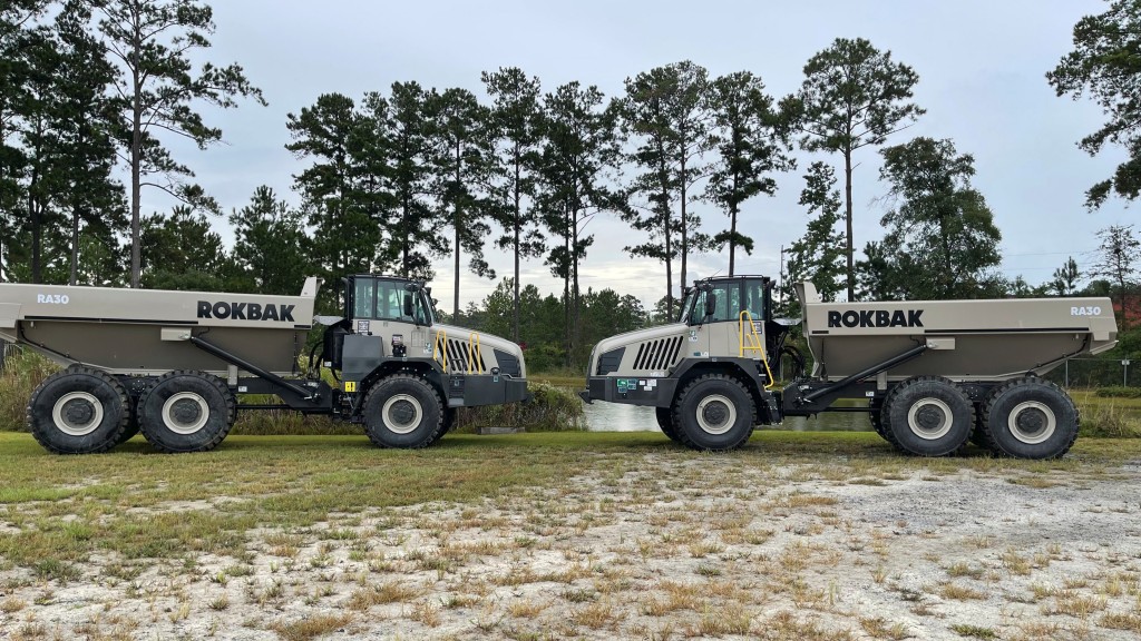 Two articulated haulers parked near a pond