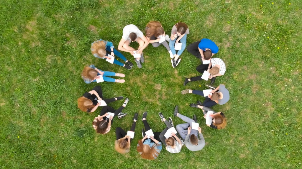 Students sit in a circle on a grassy field
