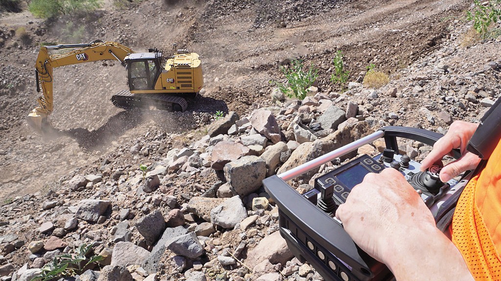 An operator looks down a hill to an excavator being run remotely.