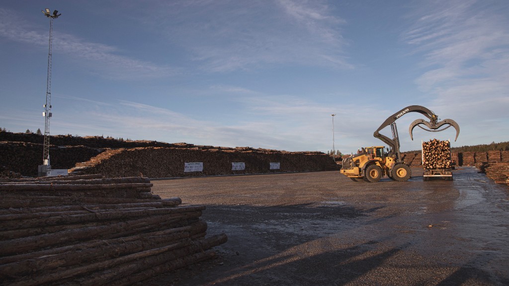 A Volvo wheel loader loads logs onto a truck