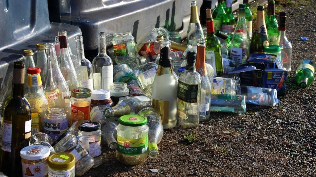 A row of used glass bottles in front of recycling bins