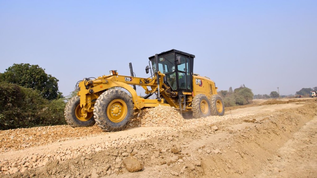 A Cat motor grader operating on a dirt and small rock filled job site