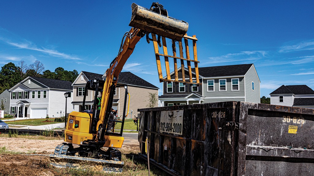 A mini excavator lifts a pallet into a dumpster