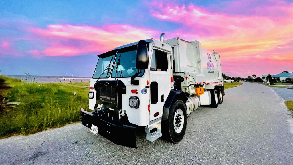 A waste collection truck with sunset behind it