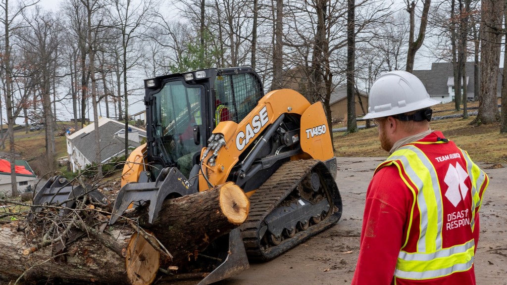 A skid steer loader moves fallen logs in a residential area