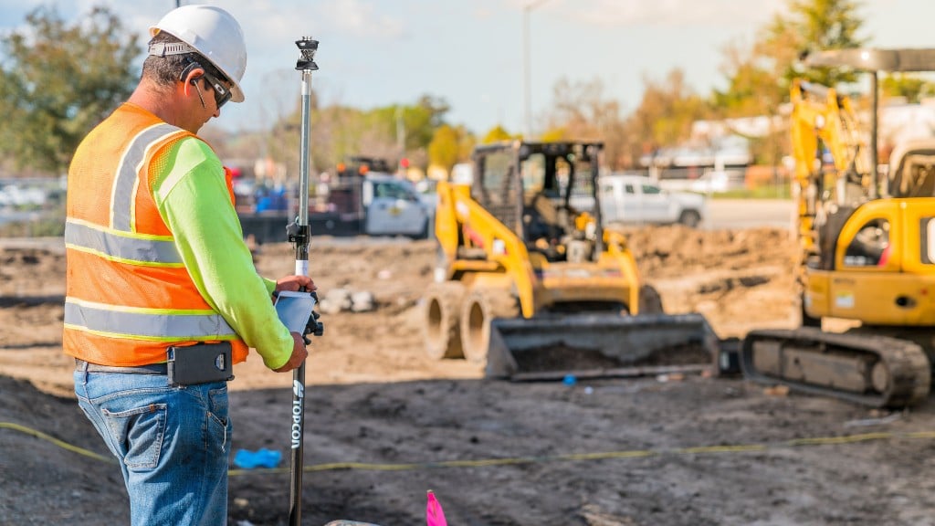 A worker using Topcon machine control equipment in front of compact machines