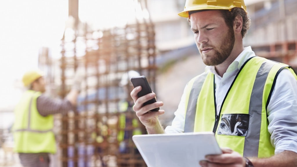 A construction worker holds a phone and tablet on the job site