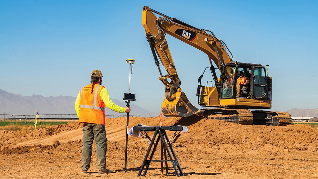 Worker uses GNSS surveying equipment on job site with excavator