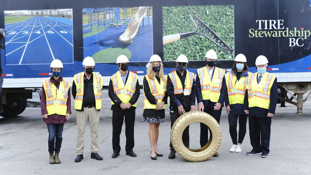 Workers in safety gear pose for a photo with a gold tire