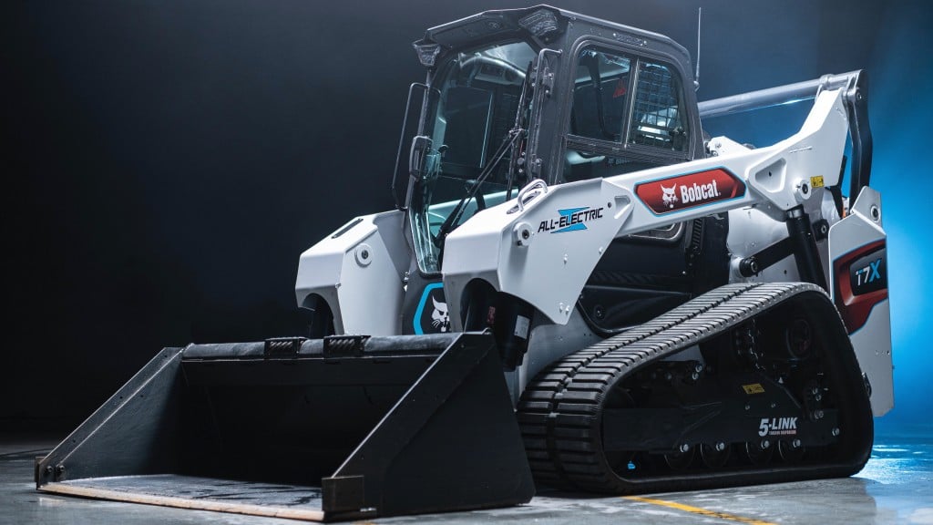 A compact track loader is parked in a dark room