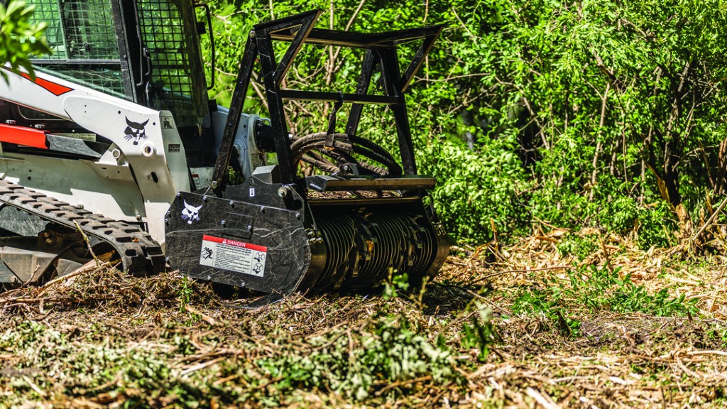 A loader drum mulcher mulches ground vegetation