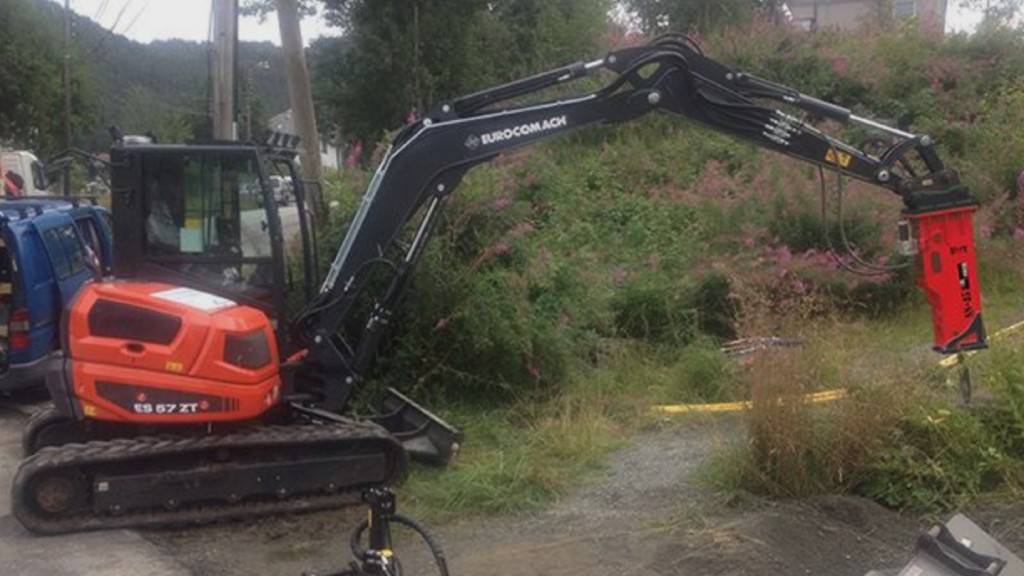 An excavator uses a hammer attachment on the job site