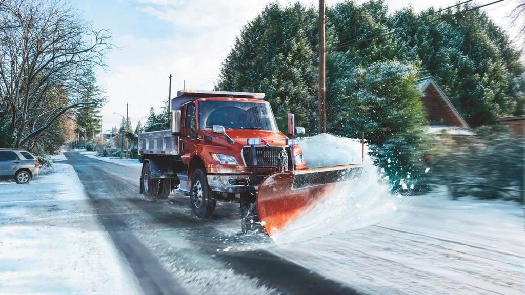 A snowplow attached to a dump truck plows a road