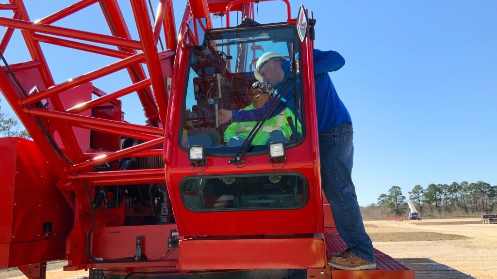 A trainer instructs an operator in the cab of a crawler crane