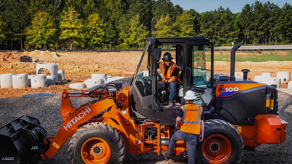 Two workers talk near the door of a wheel loader