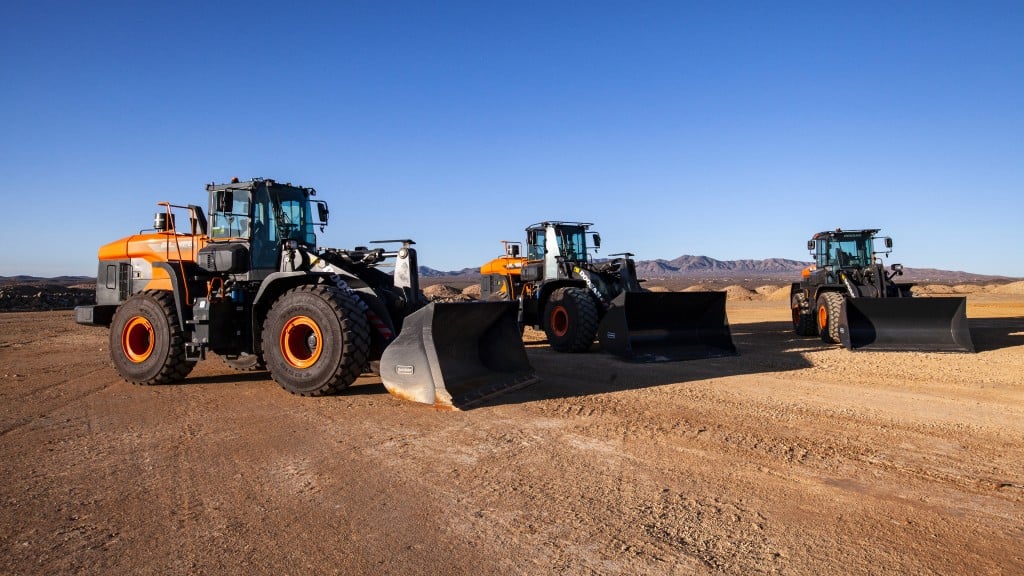 Three wheel loaders are parked in a space of flat dirt