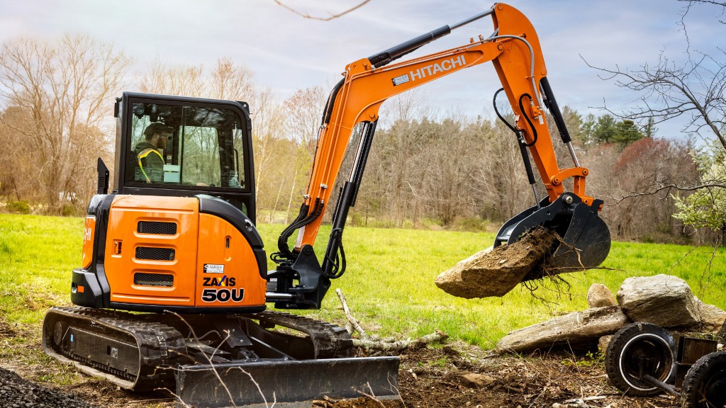 An excavator moves a large rock on a job site