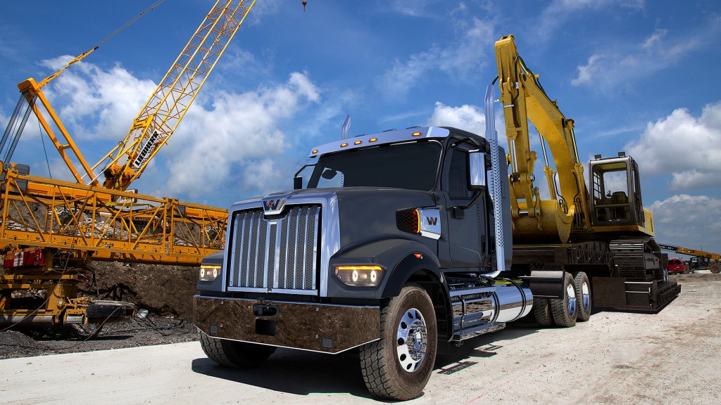 A blue truck with a flatbed trailer carrying an excavator on a work site