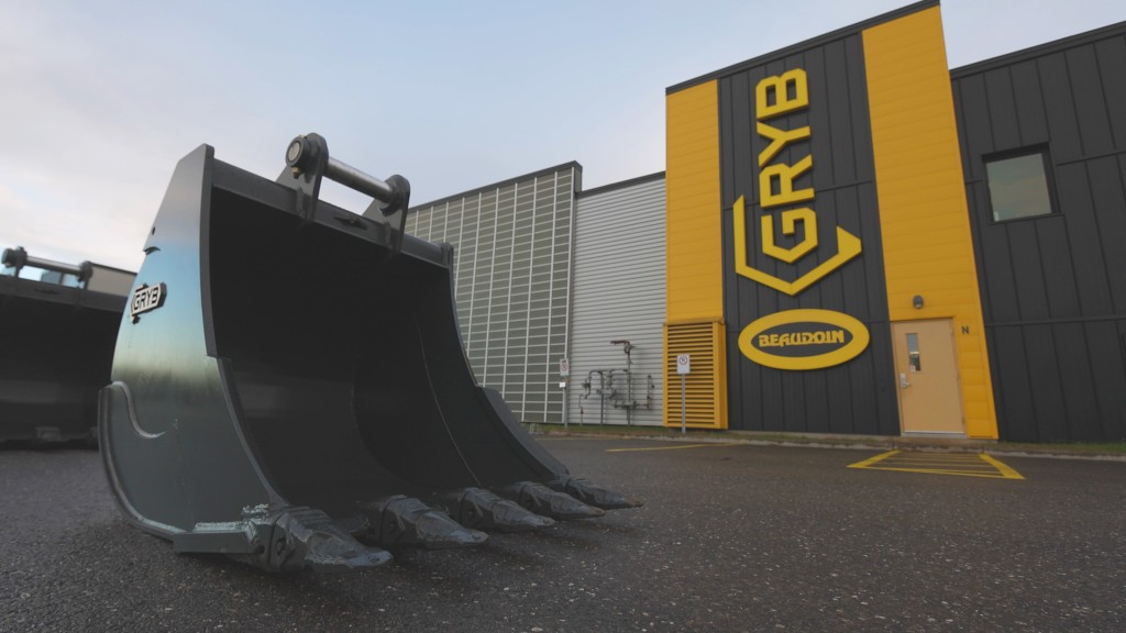 An excavator bucket sits in front of a facility