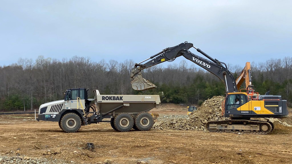 An excavator fills a hauler with rock on a job site
