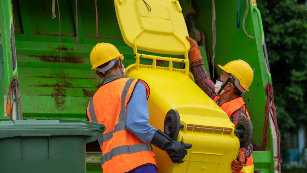 Two workers dump recyclables into a collection truck