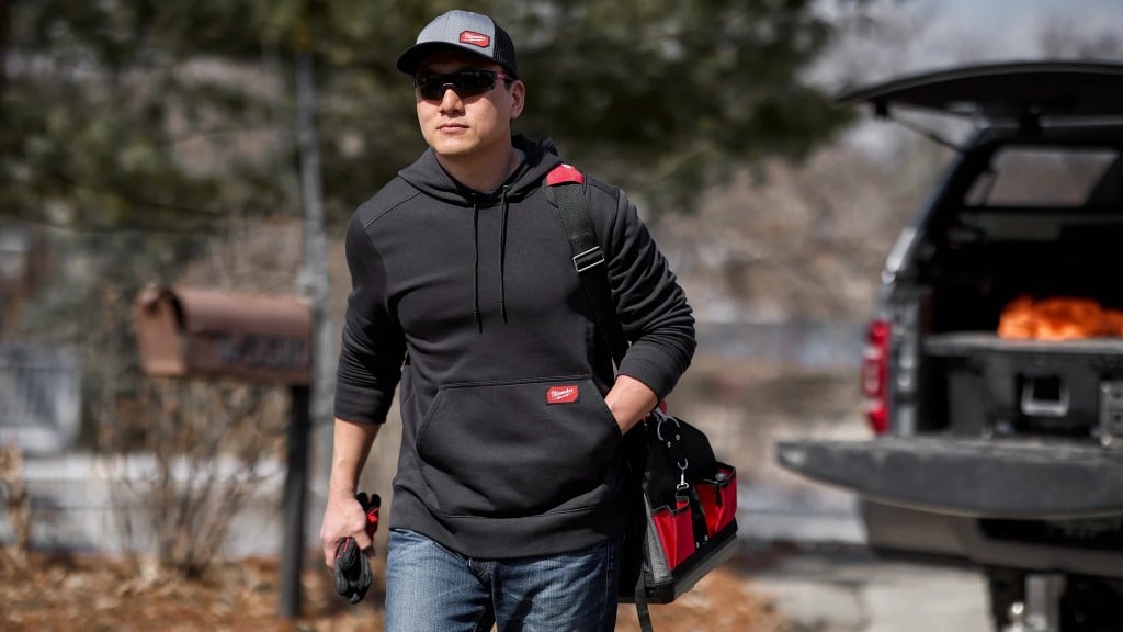 A worker walks away from an open truck cab with a bag of tools on their shoulder